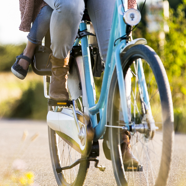 Een close up van een wiel en de benen van een vrouw en kindje op de fiets