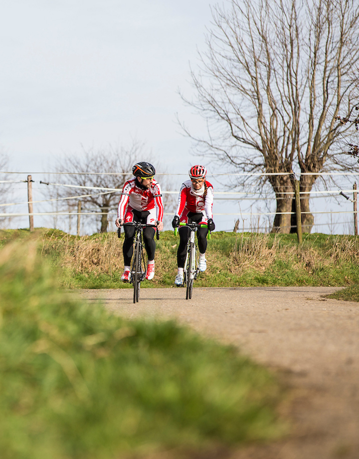 Twee wielrenners fietsen langs de kale bomen